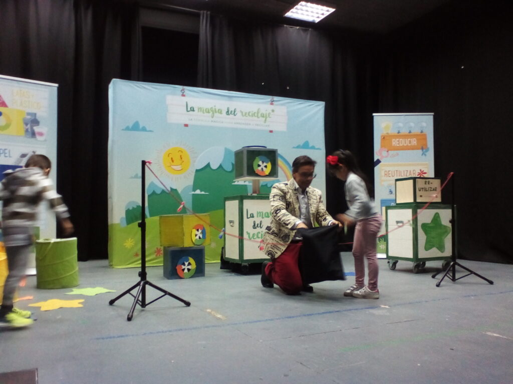 Foto donde se ve la obra de teatro reciclaje donde se ve a Manu el Mago jugando con dos niños en el escenario